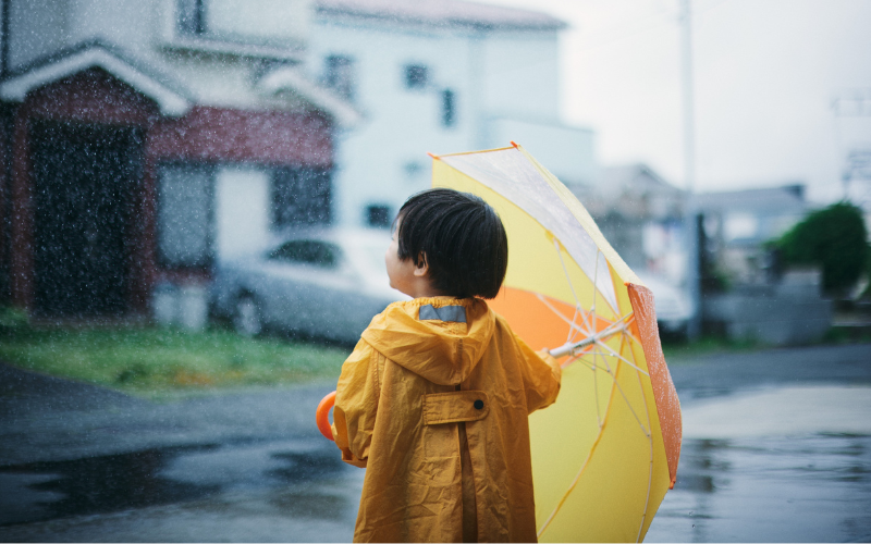 傘を持っている子供の写真。雨が降っていて空を見上げている。